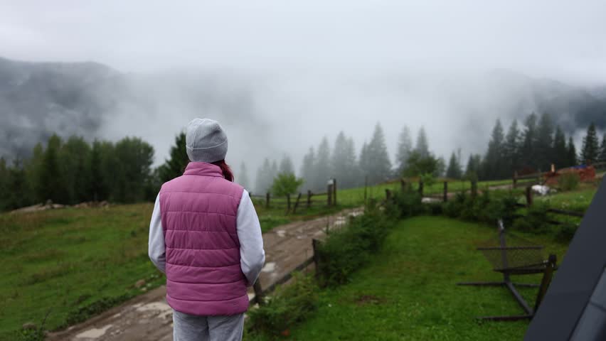 Girl stands in the Carpathian Mountains of Ukraine and looks over the landscape in the morning