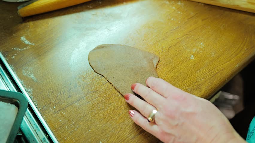Woman cuts heart-shaped gingerbread cookies from rolled dough with cookie cutter