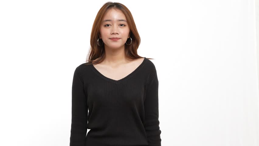 Cute young Asian woman singing or speaking into a microphone while pointing over her shoulder on a white background