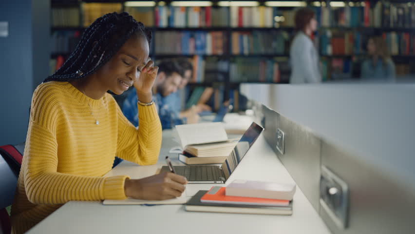 University Library Education: Gifted Black Girl uses Laptop, Writes Notes for the Paper, Essay, Study for Class Assignment. Diverse Multi-Ethnic Group of Students Learning, Studying for Exams, Talk in College