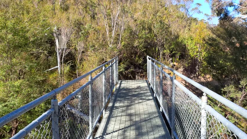 First-person perspective walking across a metal bridge on a bushland trail in Wentworth Falls.