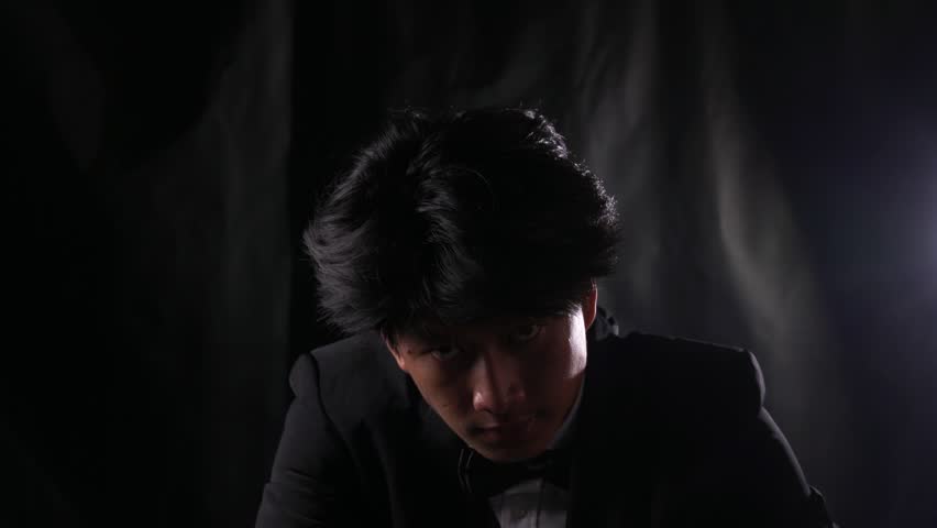 Menacing mafia hitman in a tuxedo points a smoking revolver directly at the camera in the shadows. POV concept of a dramatic assassination, organized crime execution, and cinematic thriller.
