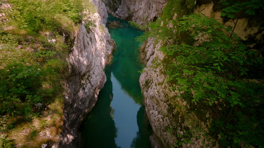 Sentiero del Dint view of limestone gorge walls with moss, green trees and a clear turquoise river, Italy.