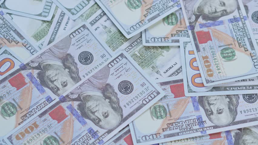 Gold bitcoin coins drop and scatter onto bed of US hundred dollar bills for cryptocurrency wealth growth concept