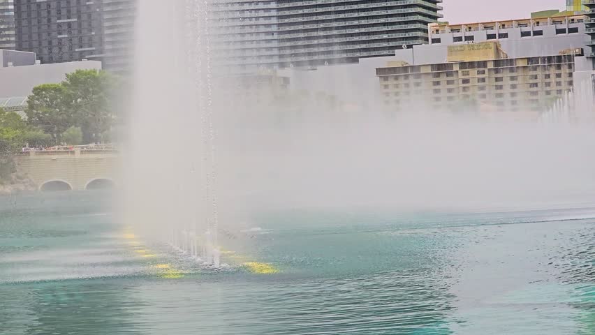 Famous Bellagio Fountains on the Las Vegas Strip, with curved water jets, mist, blue green lake, resort buildings, stone arches, rippling water, and bright city skyline backdrop for travel.