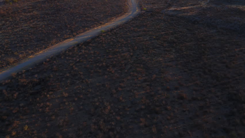 Panoramic drone reveal of Ugab Valley, Namibia at sunset. Long straight road crosses vast plain. Geological formations visible. Clear cloudless sky