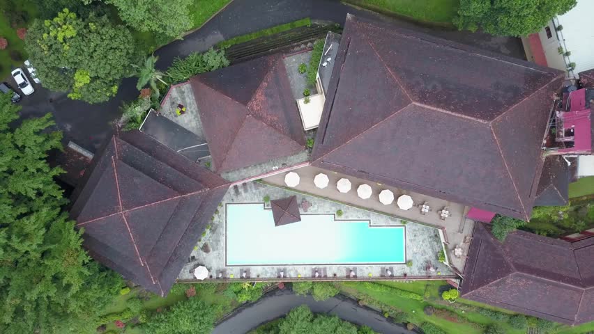 Direct top-down overhead aerial shot of a luxury hotel resort featuring a swimming pool, surrounded by a dense tropical forest canopy and winding access roads in hill country, Sri Lanka.