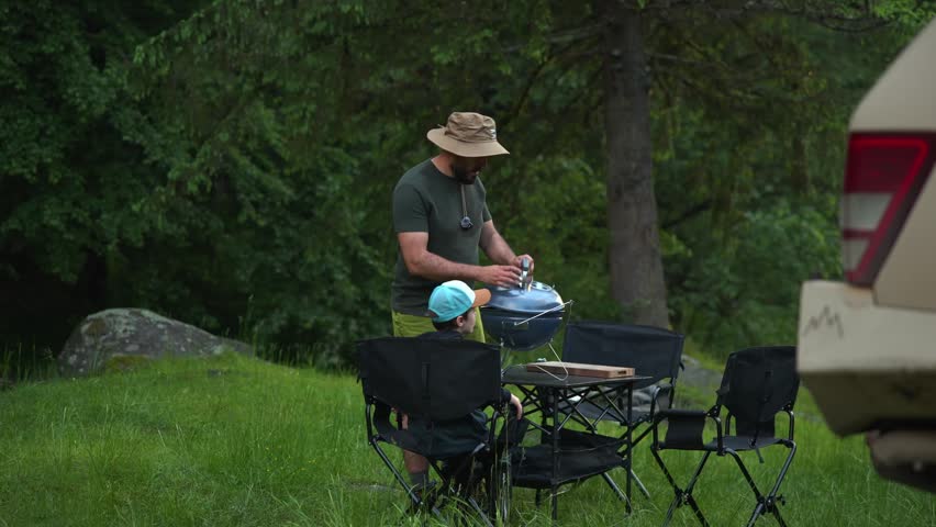 Loving father and his son enjoying a barbecue picnic in nature while overlanding on a family trip