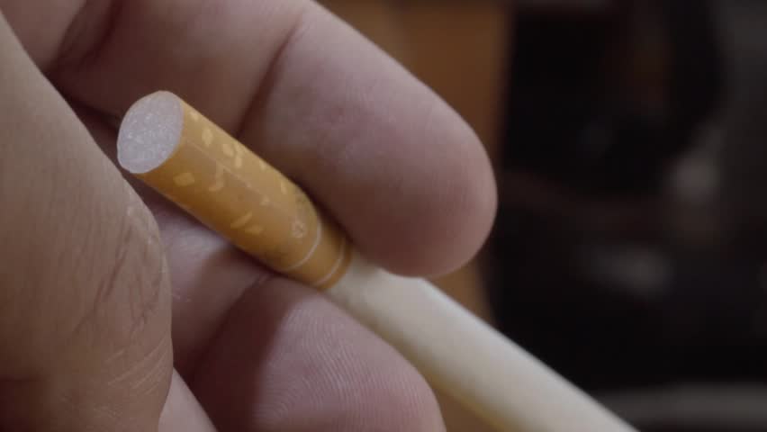 Closeup of hand holding an unlit cigar, highlighting the tobacco wrapper and cylindrical shape before lighting against dark background