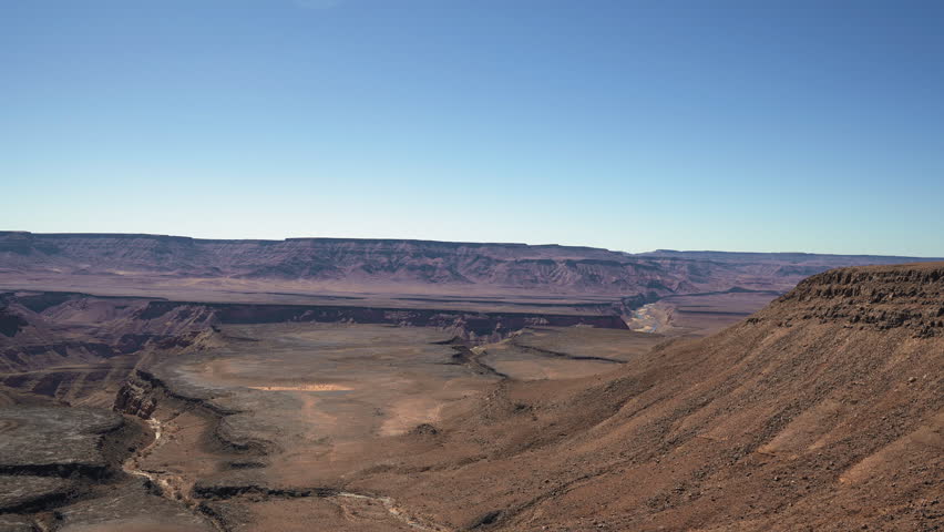 Panoramic ground shot of man standing cliff edge overlooking Fish River Canyon. Namibia, clear sky, strong midday sun