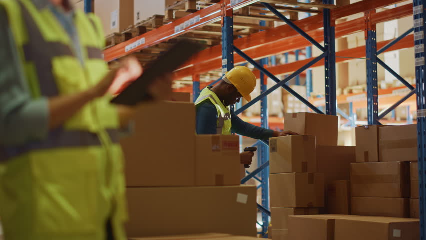 Caucasian Female Worker Uses Digital Tablet to Inspect Stock While Black Male Colleague Seals Cardboard Boxes in Retail Warehouse. E-commerce Distribution Center Preparing Online Shopping Orders