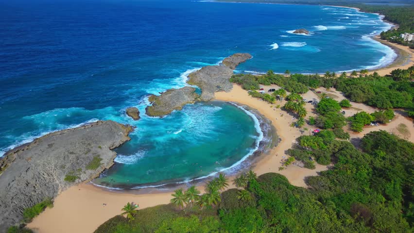 A sweeping drone view captures the famous limestone crescent cove and turquoise waters of Mar Chiquita Beach, Puerto Rico.