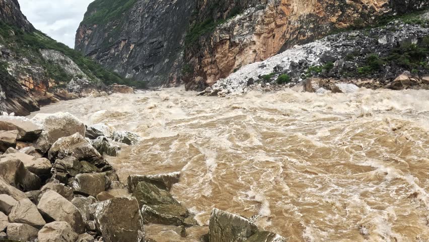 Muddy rapids roar through the narrow limestone cliffs of Tiger Leaping Gorge on the Jinsha River, filmed in slow motion, Yunnan, China.