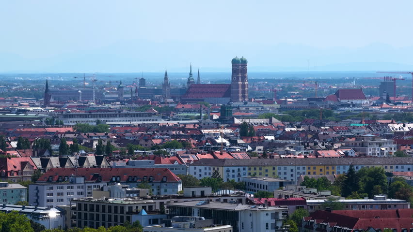 Aerial panoramic view of the Munich skyline featuring the Frauenkirche, historic church towers and iconic landmarks stretching across the Bavarian capital beneath a clear blue summer sky in Germany.