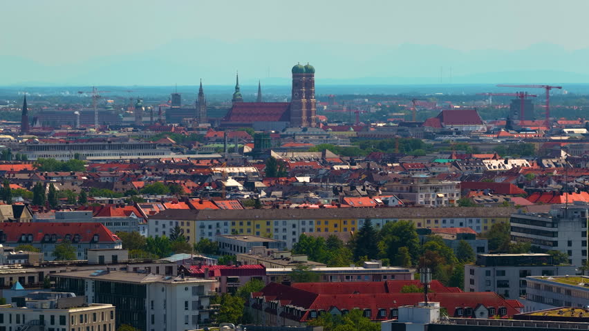Aerial panoramic view of the Munich skyline featuring the Frauenkirche, historic church towers and iconic landmarks stretching across the Bavarian capital under a clear blue sky in Germany.
