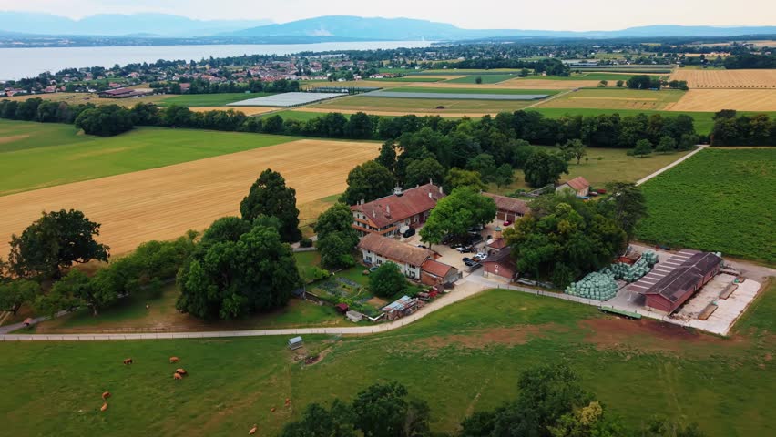Aerial view of the historic Domaine de Belle-Ferme farm surrounded by lush green fields and agricultural land in Bogis-Bossey, Vaud, Switzerland.