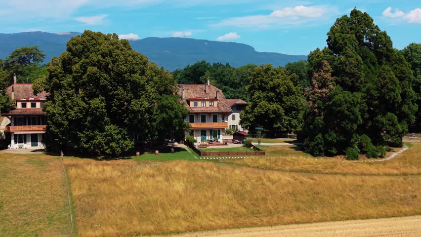 Aerial view of Domaine de Belle-Ferme surrounded by lush trees and golden fields in Bogis-Bossey, Vaud, Switzerland.