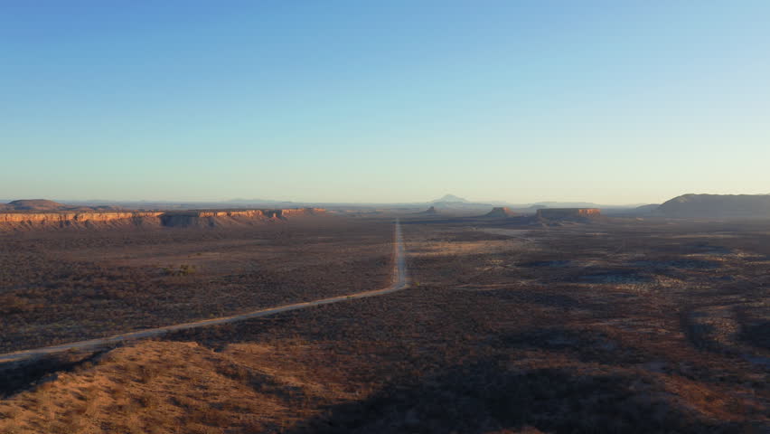 Panoramic drone view of Uganda Valley and the Ugab Terraces near Fingerklippe at sunset, showcasing a long straight road cutting through dramatic geological formations