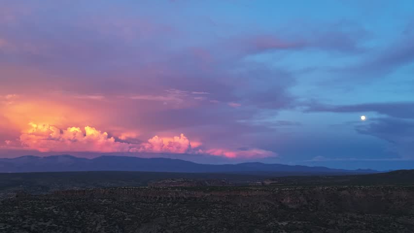 Aerial view of colorful clouds and moon rising over the vast high desert landscape in Los Alamos, New Mexico, United States.