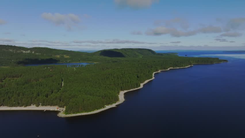 Aerial view of Koli national park with dense pine forests, rocky shoreline, and deep blue lake waters under a clear sky in Lieksa, North Karelia, Finland.