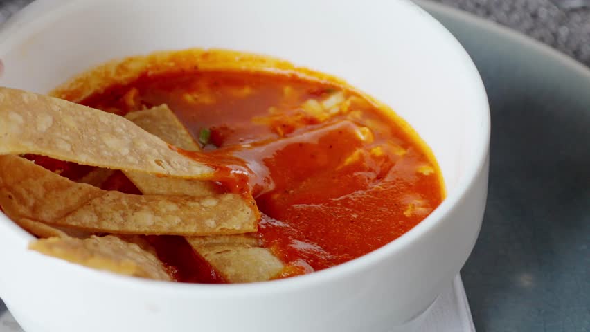 Close-up view of a person dipping a crispy tortilla chip into a delicious and warm bowl of traditional mexican sopa de tortilla, a comforting and classic dish from latin american cuisine