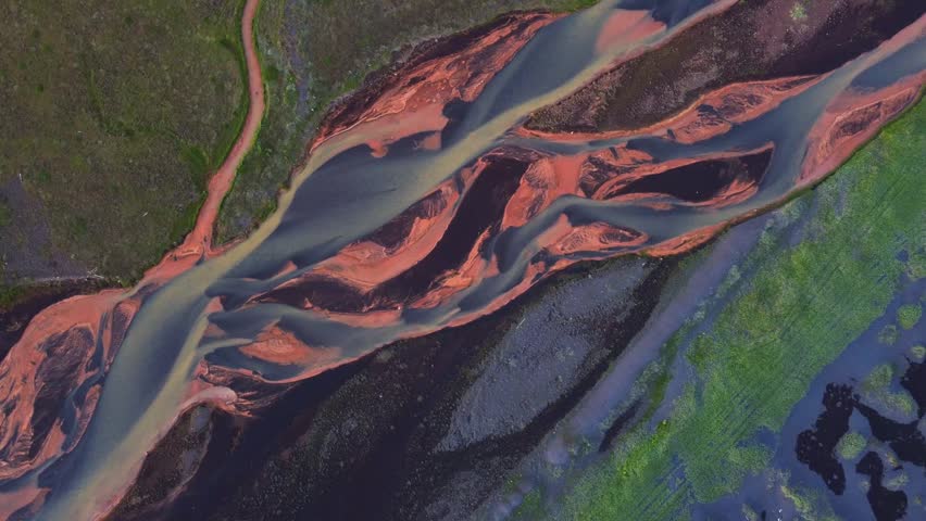 Aerial view of braided glacial river with sediment-rich channels flowing through the volcanic landscape of Iceland.