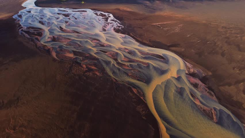 Aerial view of a winding braided glacial river flowing through the volcanic landscape of Iceland, showcasing intricate sediment patterns and golden hour light in Iceland.