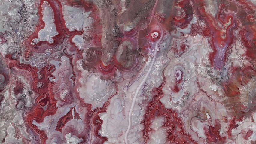 Aerial view of the colorful red and white rock formations of the badlands with a winding dirt road cutting through the desert landscape in Hanksville, Utah, United States.
