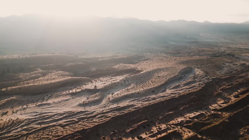 Aerial view of the arid landscape of Valles Calchaquies with rugged terrain and desert vegetation under soft sunlight in San Carlos, Salta, Argentina.