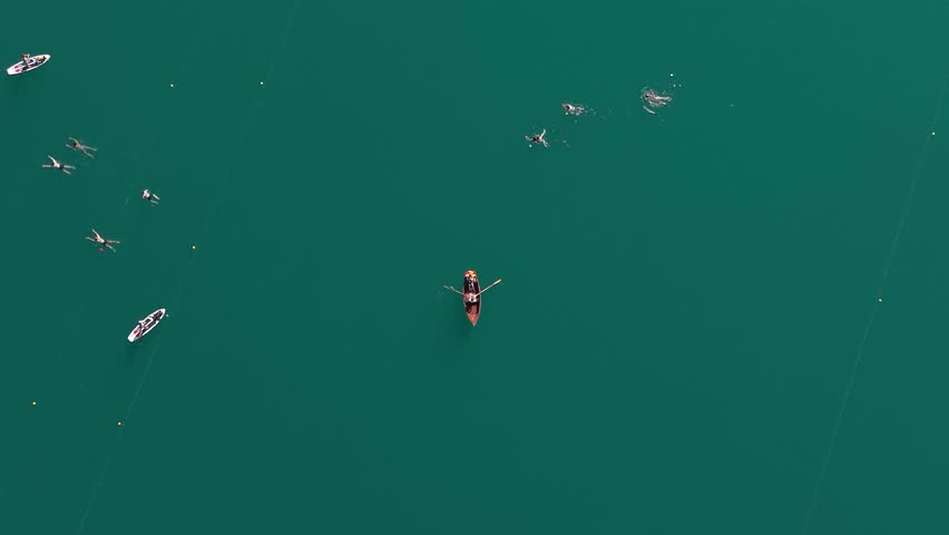 Top-down aerial view of swimmers, SUPs and row boats on Lake Bled, Slovenia