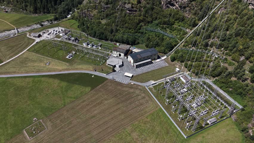 Aerial view of the Wasserkraftwerk Robbia hydroelectric power plant with its electrical substation and surrounding green fields in the valley of Poschiavo, Grisons, Switzerland.