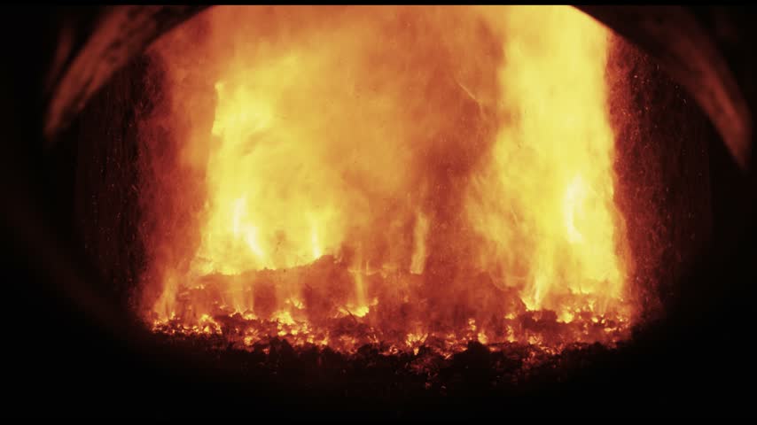 Powerful yellow orange flames fill the frame and reveal the combustion chamber of an industrial furnace in full glow. The intense fire licks over a densely glowing bed of burning fuel while the darkened rim frames the heat. This full frame close up makes the sheer energy of biomass combustion almost tangible and works as a striking background for energy and thermal process topics.