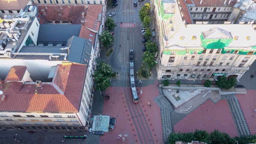 Top-down aerial view of a modern tram travelling through the historic city centre of Timișoara, Romania, crossing a pedestrian square surrounded by traditional European architecture.