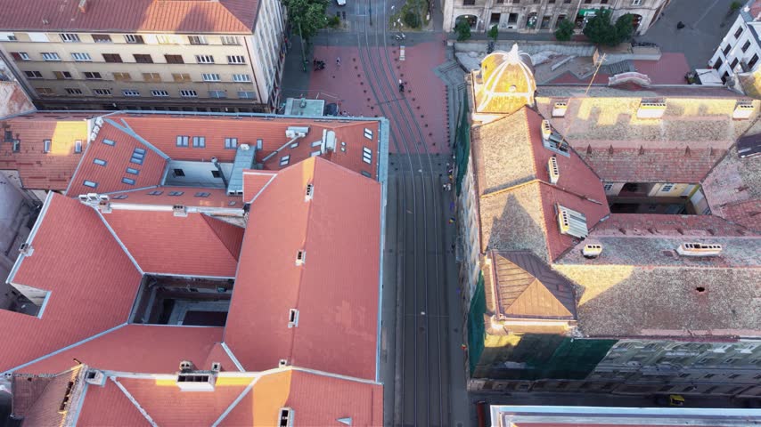 Top-down aerial view of a modern tram travelling through the historic city centre of Timișoara, Romania, crossing a pedestrian square surrounded by traditional European architecture.