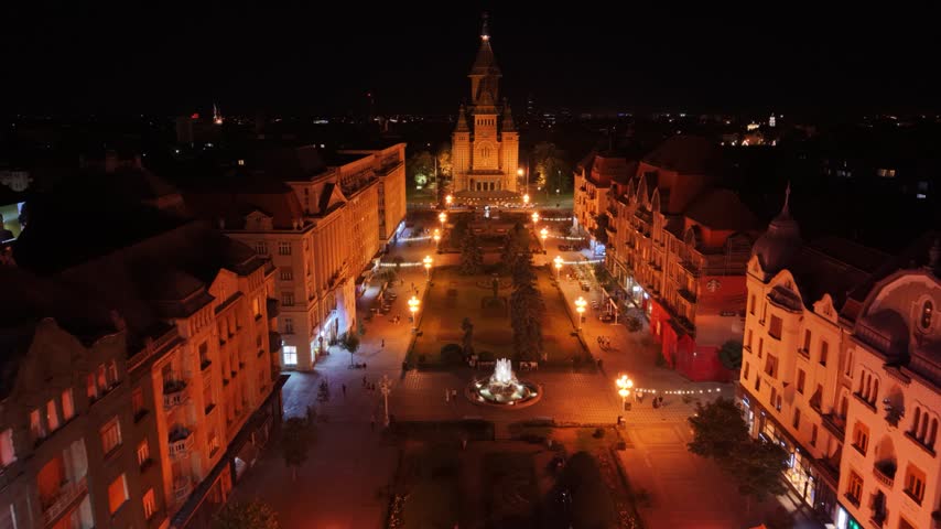Night aerial view of the illuminated Romanian Orthodox Metropolitan Cathedral in Timișoara, Romania, surrounded by city streets, traffic and urban lights in the historic city centre.