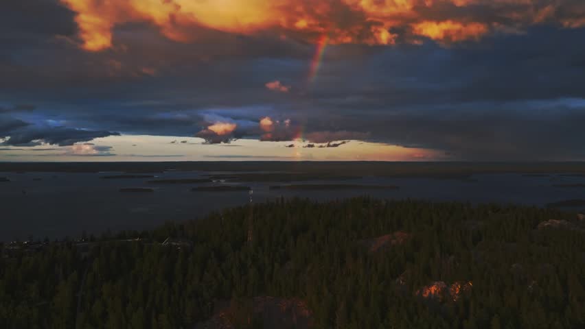 Aerial view of Koli National Park featuring a dense pine forest, a vast lake under a dramatic sunset sky with a rainbow Lieksa, North Karelia, Finland.