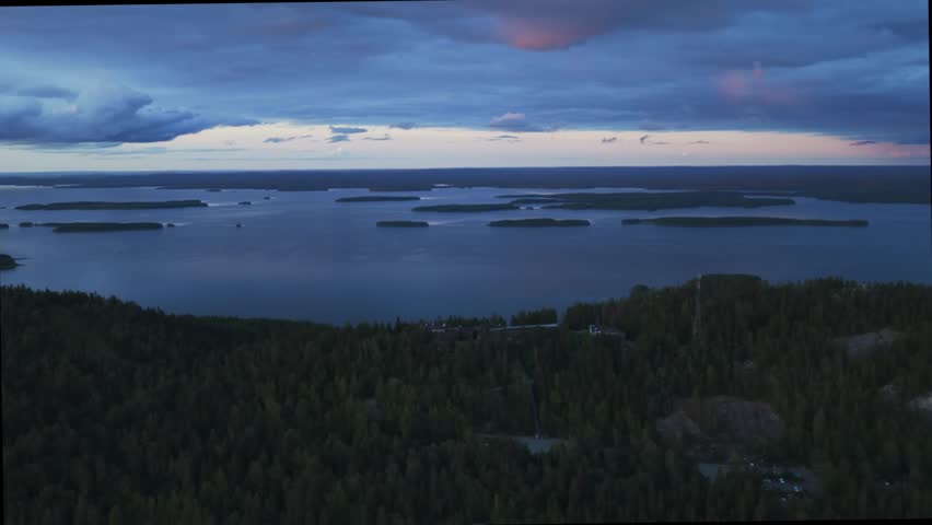 Aerial view of Koli National Park with dense pine forests and the expansive Pielinen lake under a dramatic twilight sky in Lieksa, North Karelia, Finland.
