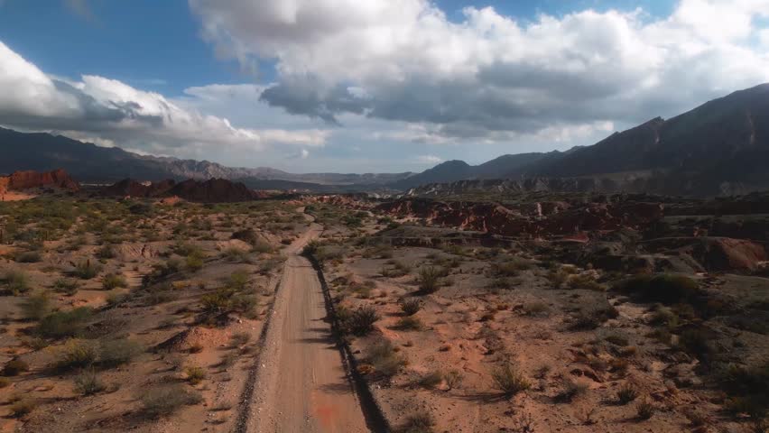 Aerial view of Valles Calchaquies with a winding dirt road cutting through the arid mountainous landscape under a cloudy sky in San Carlos, Salta, Argentina.
