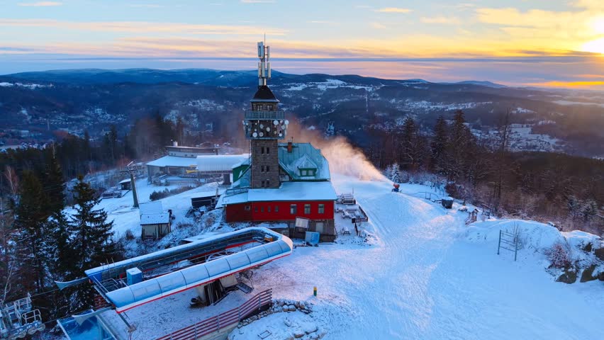 Aerial view of the Tanvaldsky Spicak observation tower and ski resort covered in snow during sunset in Tanvald, Liberecky kraj, Czechia.