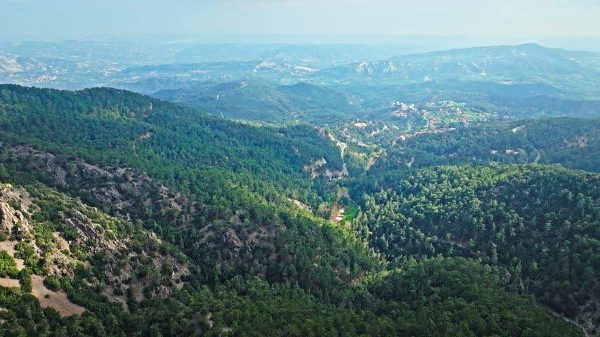 Drone view from Mount Olympus in Cyprus. Green valleys, forested hills and distant mountain ranges create a wide panoramic nature scene.