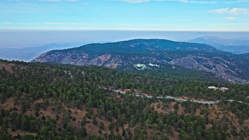 Wide aerial view from Mount Olympus in Cyprus. Forested valleys, rolling Troodos mountain ranges and distant blue hills create a peaceful panoramic landscape.