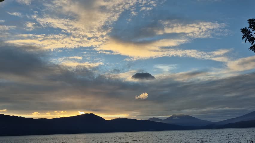 Epic sky with dramatic clouds at sunset, reflecting on a serene lake with dark, silhouetted mountain ranges in the distance.