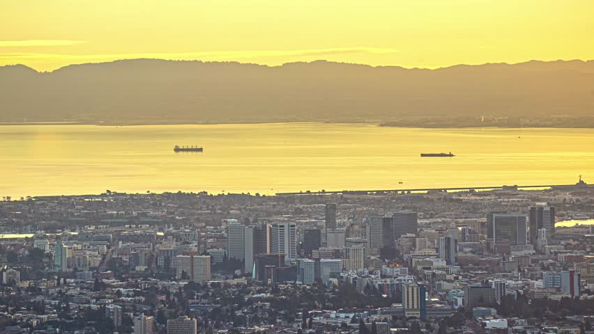 View of the San Francisco skyline at sunset with golden light reflecting on the bay and distant hills in San Francisco, California, United States.