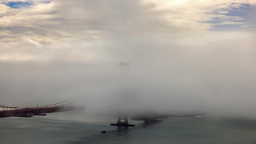 View of the iconic Golden Gate Bridge partially obscured by thick rolling fog over the bay in San Francisco, California, United States.