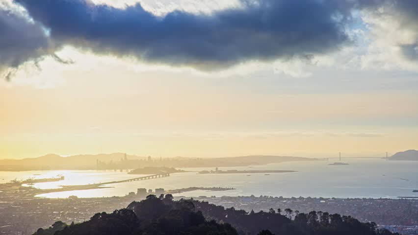 View of San Francisco skyline and the Golden Gate Bridge across the bay during sunset with dramatic clouds over the water in San Francisco, California, United States.