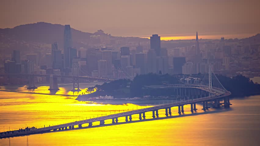 View of the San Francisco Bay Bridge and city skyline illuminated by the golden light of sunset in San Francisco, California, United States.