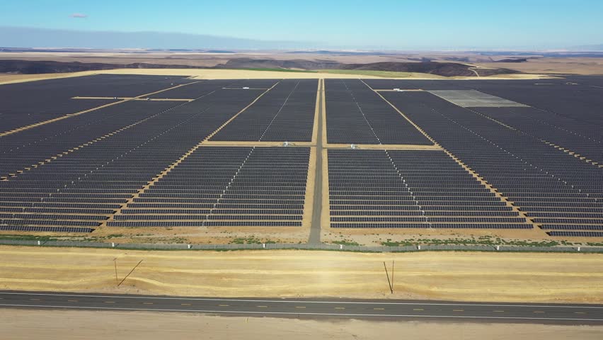 4K aerial drone footage of a large-scale solar farm with wind turbines visible in the distance near Arlington, Oregon, USA. Extensive photovoltaic solar panels and modern wind power infrastructure demonstrate two complementary forms of renewable energy generation across the dry high desert landscape. Sustainable electricity production, clean energy development and low-carbon power generation support the regional electrical grid while showcasing large-scale green energy infrastructure in the Pacific Northwest