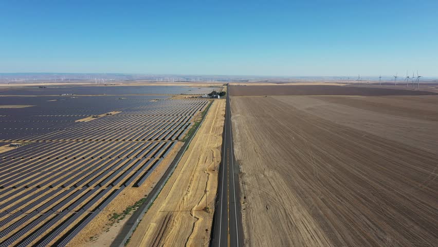 4K aerial drone footage of a large-scale solar farm with wind turbines visible in the distance near Arlington, Oregon, USA. Extensive photovoltaic solar panels and modern wind power infrastructure demonstrate two complementary forms of renewable energy generation across the dry high desert landscape. Sustainable electricity production, clean energy development and low-carbon power generation support the regional electrical grid while showcasing large-scale green energy infrastructure in the Pacific Northwest