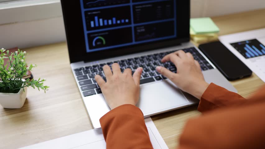 Close up of female hands working on a laptop computer with financial charts on the screen