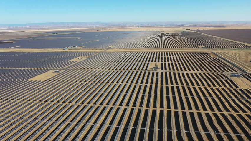 4K aerial drone footage of a large-scale solar farm with wind turbines visible in the distance near Arlington, Oregon, USA. Extensive photovoltaic solar panels and modern wind power infrastructure demonstrate two complementary forms of renewable energy generation across the dry high desert landscape. Sustainable electricity production, clean energy development and low-carbon power generation support the regional electrical grid while showcasing large-scale green energy infrastructure in the Pacific Northwest